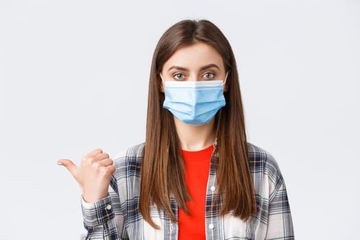 Coronavirus outbreak, leisure on quarantine, social distancing and emotions concept. Close-up of young girl in medical mask showing way, pointing thumb left at banner or information.