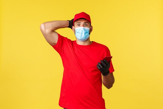 Food delivery, tracking orders, covid-19 and self-quarantine concept. Worried newbie courier first day at work, trying call client, using smartphone app, look nervous, touch head and look camera.