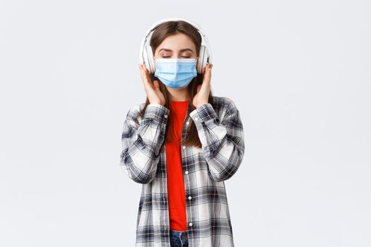 Social distancing, leisure and lifestyle on covid-19, coronavirus concept. Carefree relaxed woman in medical mask carried away with music in headphones, close eyes from satisfaction nice sound.