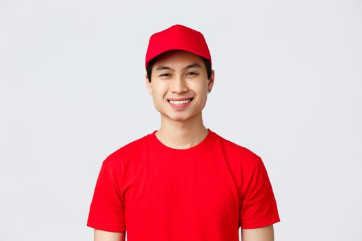 Delivery, contactless orders and shopping concept. Smiling pleasant employee of carrier service, wear uniform red cap and t-shirt, looking camera upbeat, help customer, courier transfer goods.