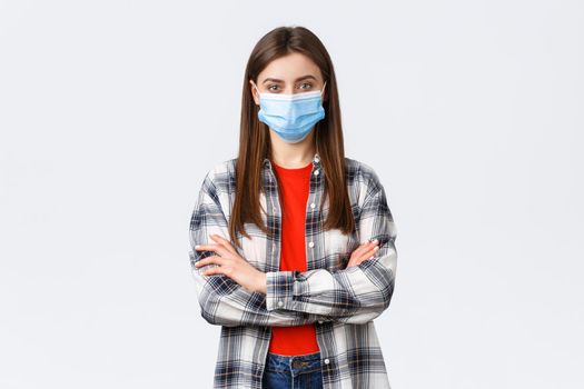 Coronavirus outbreak, leisure on quarantine, social distancing and emotions concept. Confident young woman in checked shirt wear medical mask, cross arms chest, determined look camera.