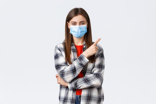 Coronavirus outbreak, leisure on quarantine, social distancing and emotions concept. Happy smiling young woman in medical mask provide information on covid-19 pointing finger upper right.