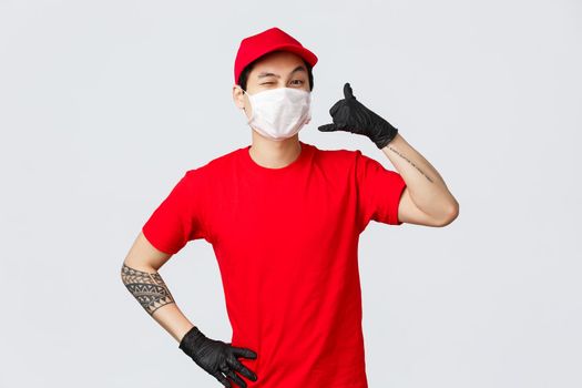Happy asian delivery guy in medical mask tell give call, wink cheeky to client, keep in touch when delivery needed, fast shipment, good quality of courier services, safe shopping during pandemic.