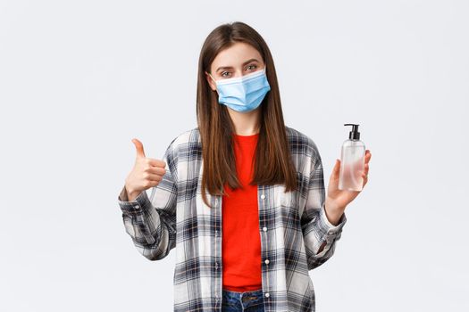 Coronavirus outbreak, leisure on quarantine, social distancing and emotions concept. Cheerful pleased young girl recommend hand-sanitizer brand, thumb-up, wear medical mask.