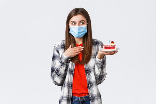 Coronavirus outbreak, lifestyle during social distancing and holidays celebration concept. Dreamy happy young girl in medical mask celebrating birthday, hold b-day cake, think what wish.