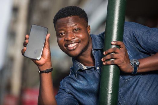 young african man behind iron bar with mobile phone looking at camera smiling.