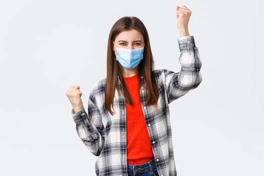 Different emotions, covid-19 pandemic, coronavirus self-quarantine and social distancing concept. Excited charismatic young woman in medical mask celebrate victory, dancing in rejoice, raise hands up.