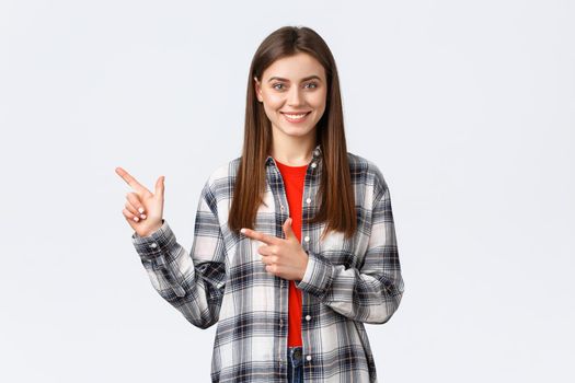 Lifestyle, different emotions, leisure activities concept. Pleasant smiling brunette girl in checked shirt, pointing fingers left, showing way to promo, recommend click link or buy product.