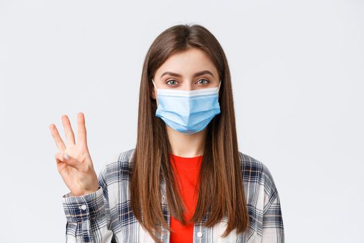 Coronavirus outbreak, leisure on quarantine, social distancing and emotions concept. Close-up of cheerful attractive woman in medical mask show number three, third, white background.