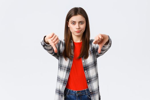 Lifestyle, different emotions, leisure activities concept. Skeptical and disappointed young woman smirk unsatisfied and showing thumbs-down in dislike, disapprova and judging bad product.