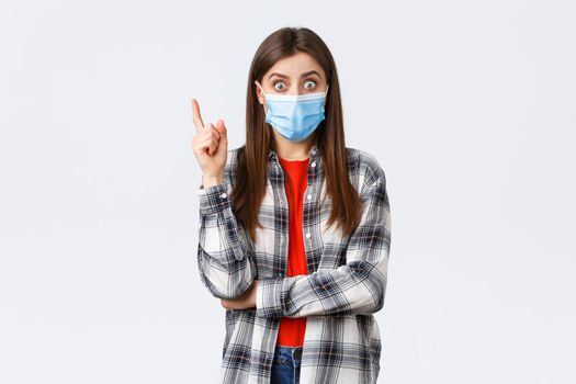 Coronavirus outbreak, leisure on quarantine, social distancing and emotions concept. Excited smart young woman in medical mask and checked shirt, raising index finger to say suggestion, have idea.