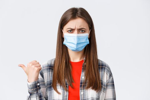 Coronavirus outbreak, leisure on quarantine, social distancing and emotions concept. Upset and disappointed young woman in medical mask frowning, condemn smth, pointing finger left displeased.