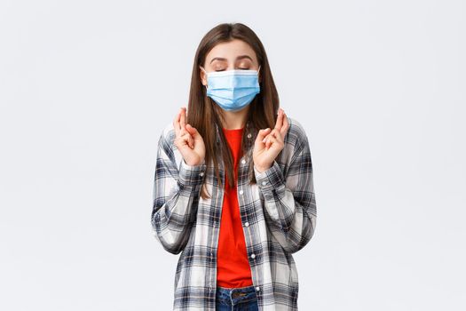 Coronavirus outbreak, leisure on quarantine, social distancing and emotions concept. Hopeful cute young woman in medical mask praying, close eyes and cross fingers good luck, making wish.