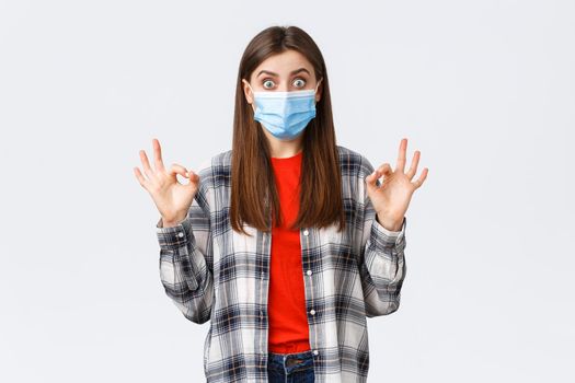 Coronavirus outbreak, leisure on quarantine, social distancing and emotions concept. Excited and surprised young woman showing okay sign as see really good promo, wear medical mask.