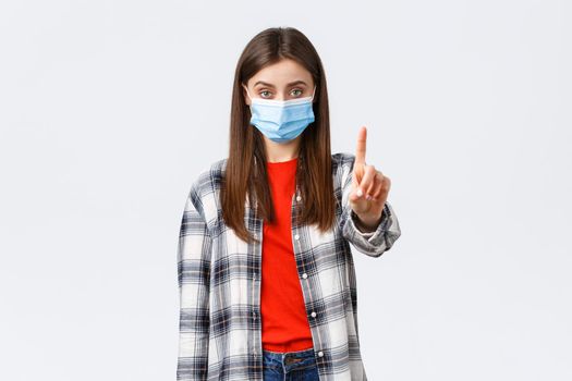 Coronavirus outbreak, leisure on quarantine, social distancing and emotions concept. Serious young woman, elder sister in medical mask shaking finger in stop, prohibition, stay home.