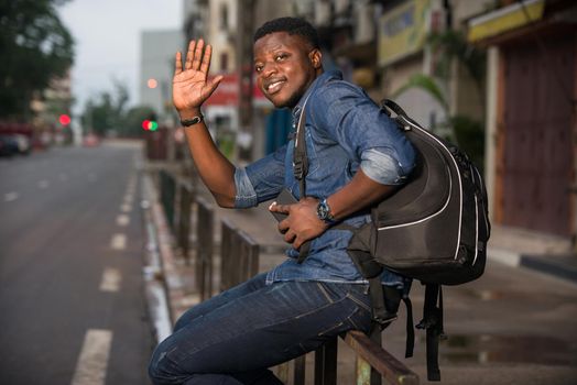 young man sitting in jeans on iron bar greeting smiling.