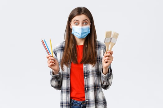 Social distancing, leisure and hobbies on covid-19 outbreak, coronavirus concept. Excited cheerful girlfriend suggest drawing together, holding painting brushes and colored pencils, wear medical mask.