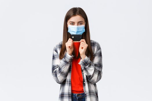 Coronavirus outbreak, working from home, online shopping and contactless payment concept. Girl in medical mask smiling sly and showing credit card, ready waste all money in internet stores.