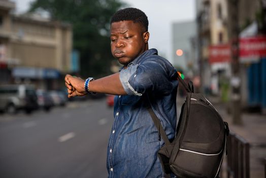 young man standing in jeans backpack watching his watch.