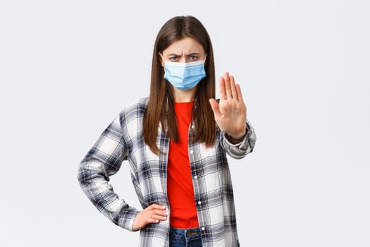 Coronavirus outbreak, leisure on quarantine, social distancing and emotions concept. Young woman in medical mask look disappointed, disapprove smth, show stop or prohibition gesture.