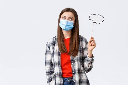 Coronavirus outbreak, leisure on quarantine, social distancing and emotions concept. Thoughtful smart young girl in medical mask searching for inspiration, thinking, holding commend cloud.