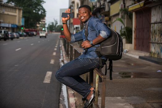 young man sitting on iron bar with backpack greeting smiling.