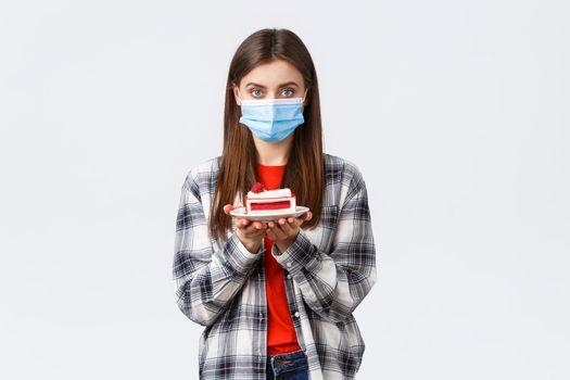 Coronavirus outbreak, lifestyle during social distancing and holidays celebration concept. Young cute girl in medical mask and casual outfit, holding birthday cake and looking serious camera.