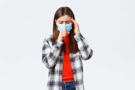 Coronavirus outbreak, leisure on quarantine, social distancing and emotions concept. Young woman feel sick, wear medical mask and coughing, touch temple as headache, high fever.