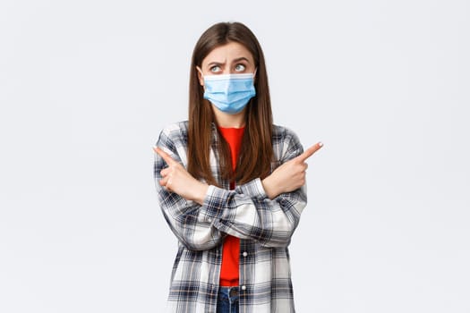 Coronavirus outbreak, leisure on quarantine, social distancing and emotions concept. Indecisive young woman making choice. Girl in medical mask puzzled facing decision, point sideways, think.