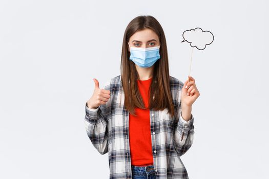 Coronavirus outbreak, leisure on quarantine, social distancing and emotions concept. Pleased young determined girl in medical mask thumb-up, hold bubble commend cloud on stick.