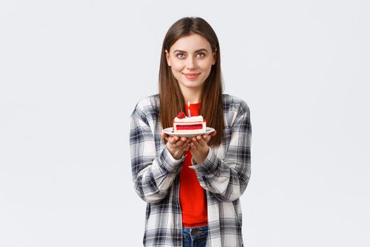 People lifestyle, holidays and celebration, emotions concept. Happy attractive girl looking up, imaging dream come true, making wish holding birthday cake with lit candle, white background.