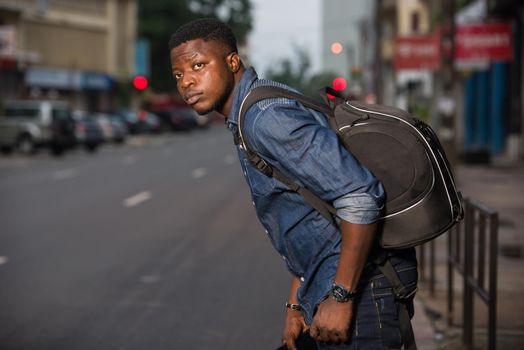 young man standing in jeans backpack and looking at his left side of the road.