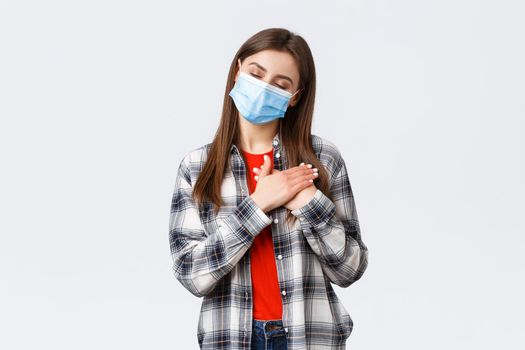Coronavirus outbreak, leisure on quarantine, social distancing and emotions concept. Dreamy attractive young woman in medical mask, close eyes imaging or remember memory, press hands to heart.