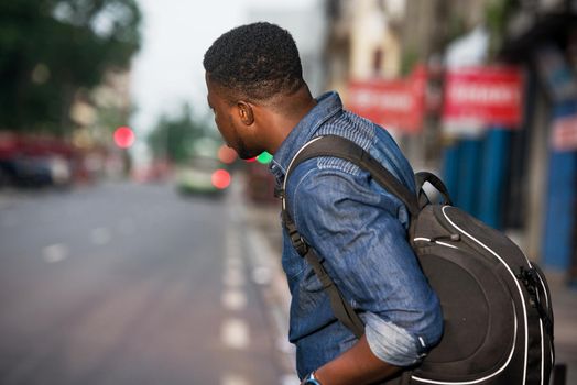 young man standing in jeans backpack watching at his right side of the road.