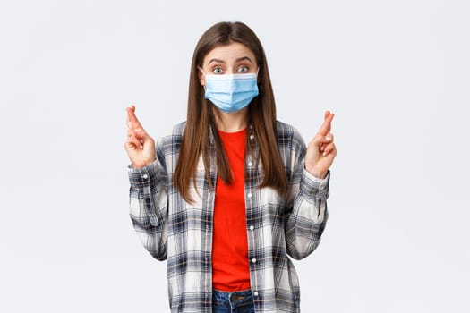 Coronavirus outbreak, leisure on quarantine, social distancing and emotions concept. Hopeful optimistic cute girl in medical mask have faith, cross fingers good luck, making wish or praying.