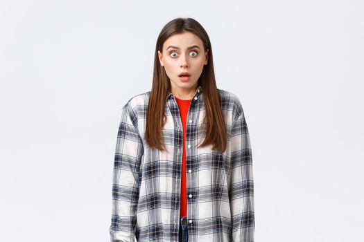 Lifestyle, different emotions, leisure activities concept. Shocked and scared, startled young woman in checked casual shirt, staring terrified, see something scary, standing in stupor.