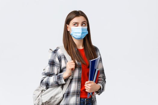 Coronavirus pandemic, covid-19 education, and back to school concept. Smart female student, freshman girl heading to class, look upper left corner interested at banner, hold notebooks and backpack.