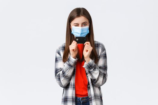 Coronavirus outbreak, working from home, online shopping and contactless payment concept. Cheerful pretty woman in medical mask showing credit card and wink sassy.