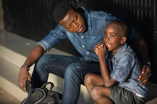 Cute little boy and his father are waiting for bus on the platform of the train station. Travel, tourism, vacation and family concept. Man and his son together sitting outside.