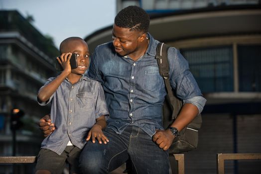 Father and son sitting in the street waiting for a car, young child talking on the cell phone beside his father. concept of tourist and travel with children.