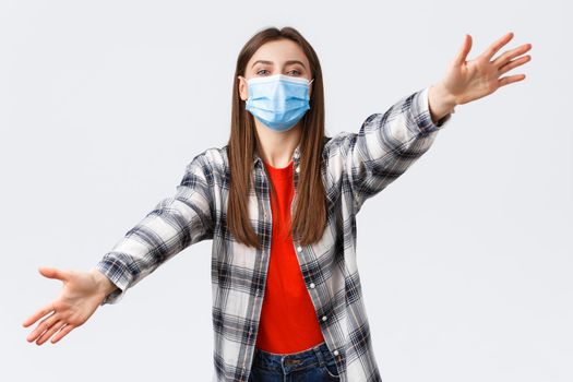 Coronavirus outbreak, leisure on quarantine, social distancing and emotions concept. Cute young woman in medical mask on self-isolation with family, spread hands sideways, dreaming of hugging you.