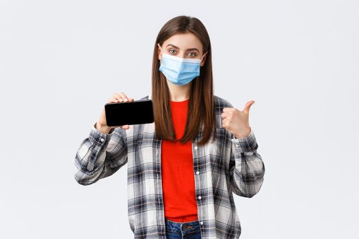 Different emotions, covid-19, social distancing and technology concept. Satisfied smiling girl in medical mask, show thumb-up and mobile phone screen, recommend application or link.