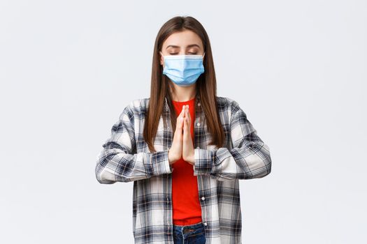 Different emotions, covid-19 pandemic, coronavirus self-quarantine and social distancing concept. Patient and calm young woman in medical mask, praying, meditating with palms together and closed eyes.