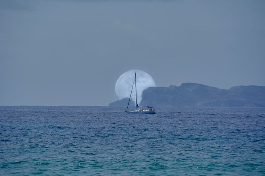 Full moon rising behind island and sailboat.Mediterranean Sea. Balearic Islands. Front view, empty space