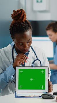 Doctor and patient looking at green screen on tablet for annual checkup visit. Medic holding modern gadget with isolated background and mockup template for chroma key on display.