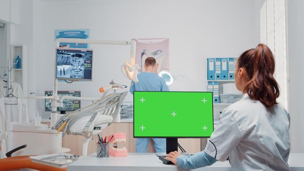 Dentist using green screen on monitor and talking to man assistant in oral care cabinet. Woman working with mockup template and chroma key on computer for teethcare and dentition