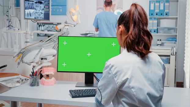 Dentist working with horizontal green screen on monitor at desk while talking to man assistant for dental care. Woman using computer with chroma key and isolated template for dentistry