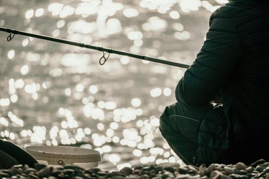 Man hobby fishing on sea tightens a fishing line reel of fish summer. Calm surface sea. Close-up of a fisherman hands twist reel with fishing line on a rod. Fishing in the blue sea outdoors