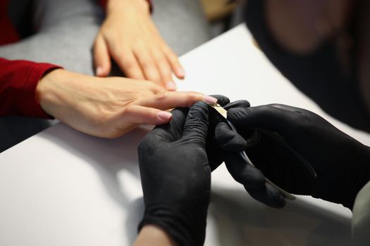 Close-up of nail master cutting off cuticle on clients hands with special equipment. Professional work in black gloves. Beauty industry, wellness concept