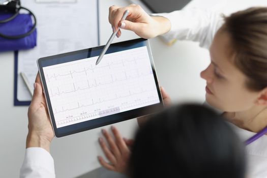 Close-up of doctor show digital tablet screen with heart cardiogram result to coworker. Examination of cardiovascular system. Medicine, cardiology concept